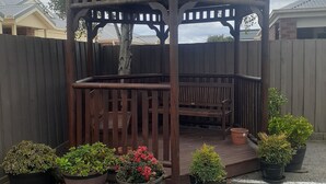 A wooden gazebo with a bench, surrounded by potted plants and a wooden fence. - City Gardens Motel Traralgon (Traralgon)