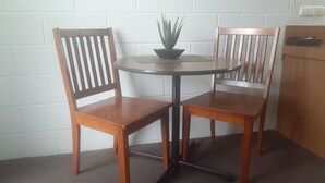 A small round table with two wooden chairs, a potted plant, and a white brick wall. - City Gardens Motel Traralgon (Traralgon)