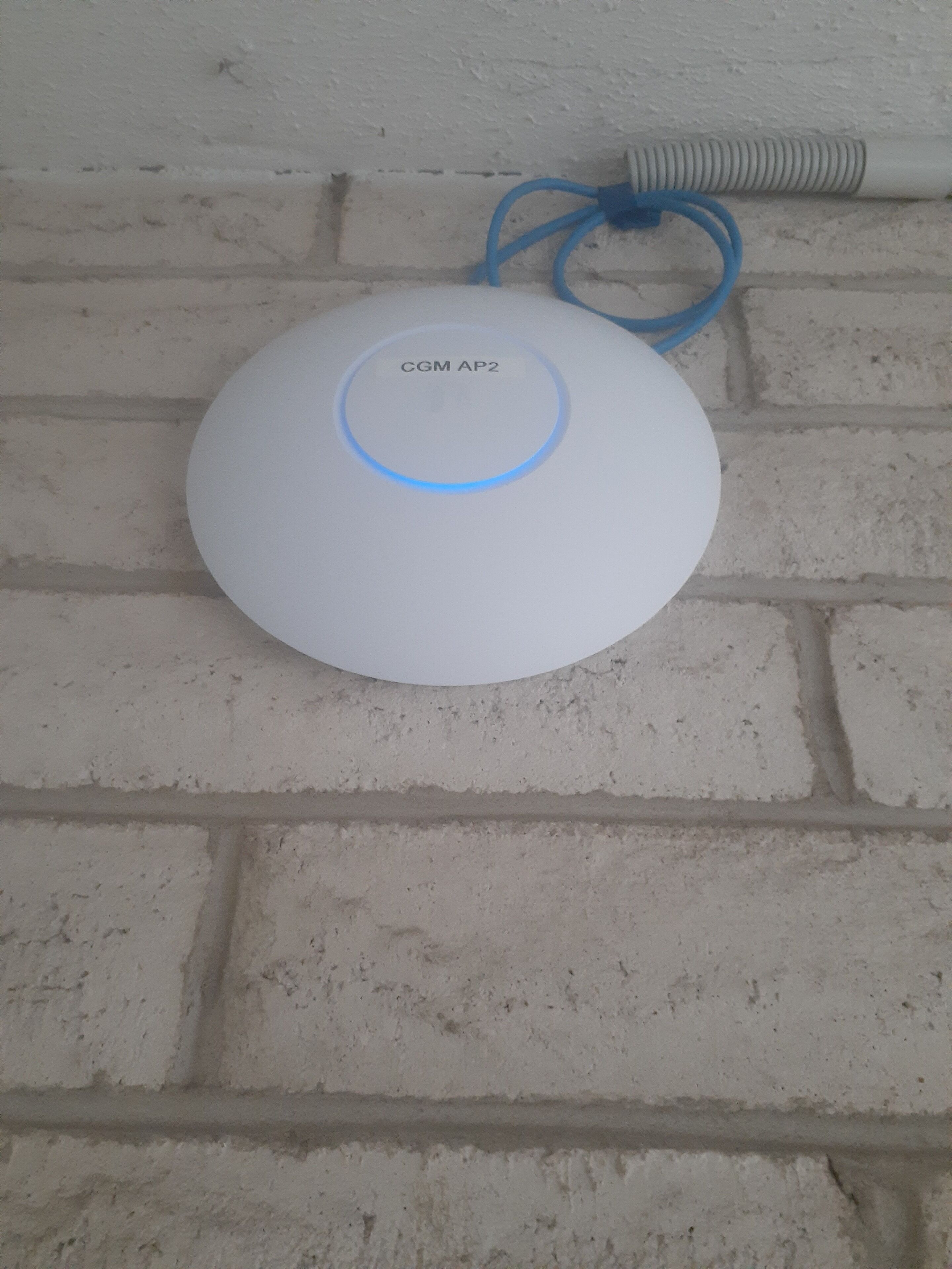 A white CGM AP2 device on a brick wall.