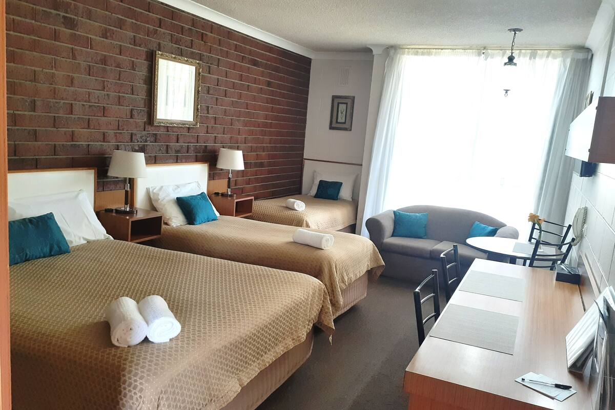 A hotel room with two beds, a sofa, a small table, and a desk.