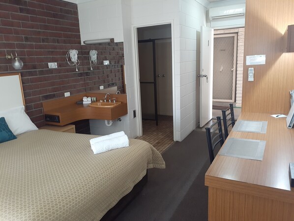 A hotel room with a bed, a wooden vanity with a sink, a mirror, and a door leading to a bathroom.
