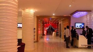 A hotel lobby with a reception desk, a television screen, and a red curtain backdrop. - Hotel Ambica Sea Green (Visakhapatnam)