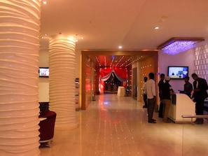 Un hall d’hôtel avec un comptoir d’accueil, un écran de télévision et un fond rouge en forme de rideau.