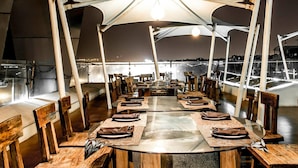 A dining area with round tables, wooden chairs, and a tent-like structure overhead. - Hotel Ambica Sea Green (Visakhapatnam)
