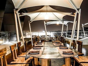 Un espace repas avec des tables rondes, des chaises en bois et une structure en forme de tente au-dessus.