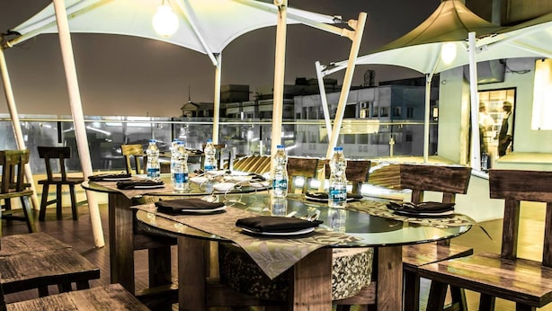 An outdoor dining area with round tables, chairs, and umbrellas providing shade. - Hotel Ambica Sea Green (Visakhapatnam)