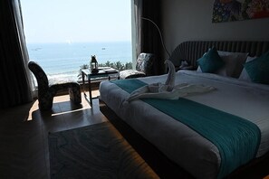 Une chambre d’hôtel avec un lit, une vue sur l’océan, une chaise et une table avec une lampe.