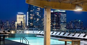 A rooftop pool area with lounge chairs and a view of the city skyline at night. - Luxy Suites Washington (Jersey City)