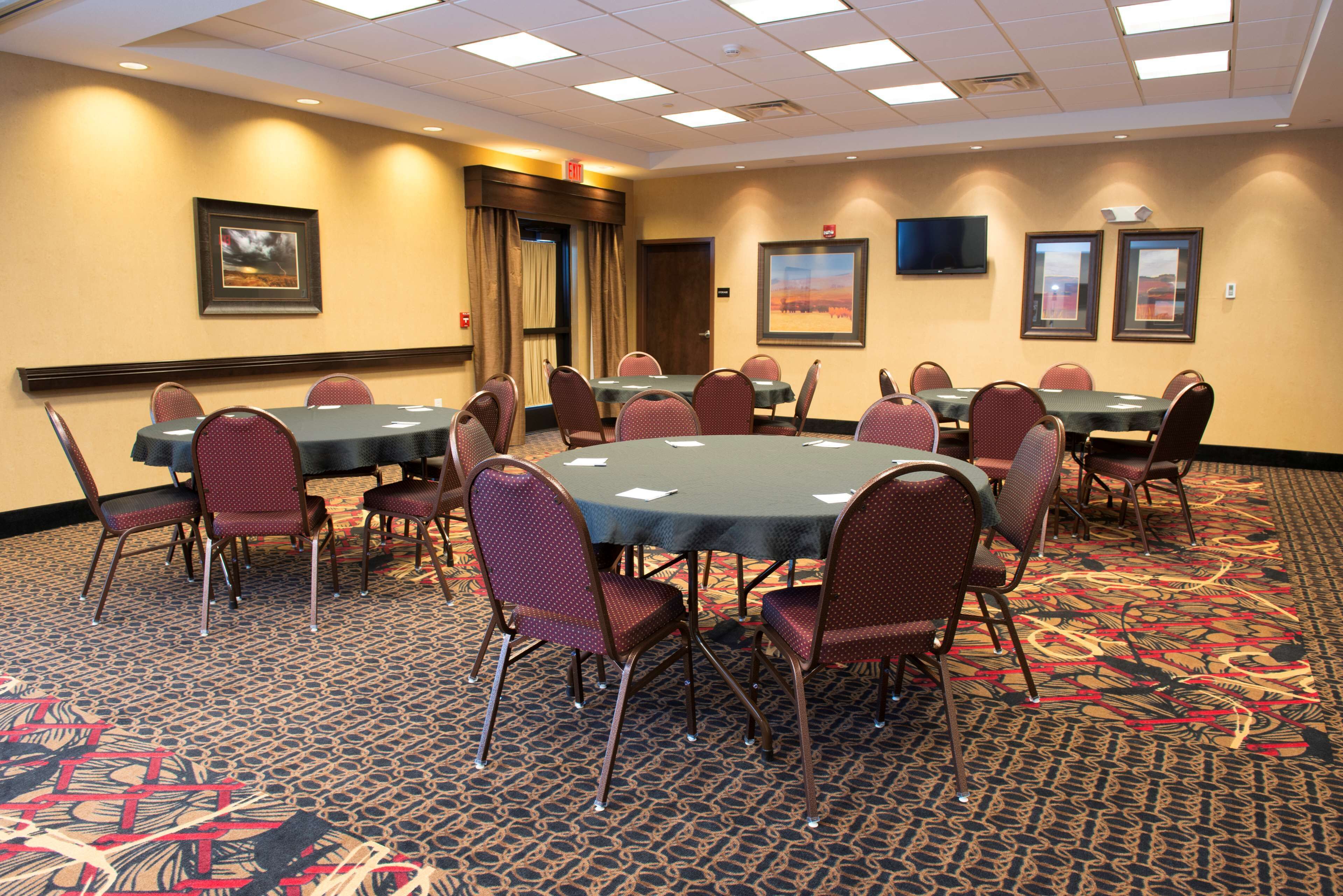 Une salle de conférence avec des tables et des chaises rondes, un sol recouvert de moquette et des tableaux encadrés aux murs.
