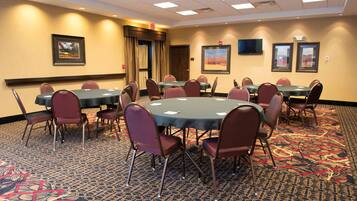 Une salle de conférence avec des tables et des chaises rondes, un sol recouvert de moquette et des tableaux encadrés aux murs.