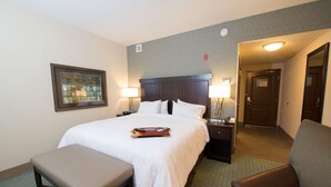 A hotel room with a large bed, two bedside tables with lamps, a bench, and a framed picture on the wall. - Hampton Inn & Suites Bismarck Northwest (Bismarck)