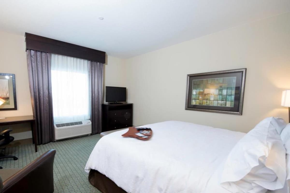A hotel room with a bed, a desk, a chair, a television, and a window with curtains.