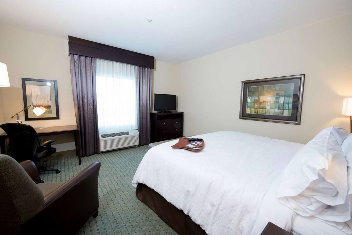 A hotel room with a bed, a desk, a chair, a television, and a window with curtains.
