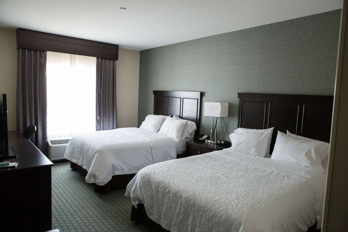 A hotel room with two beds, a desk, and a window with curtains.