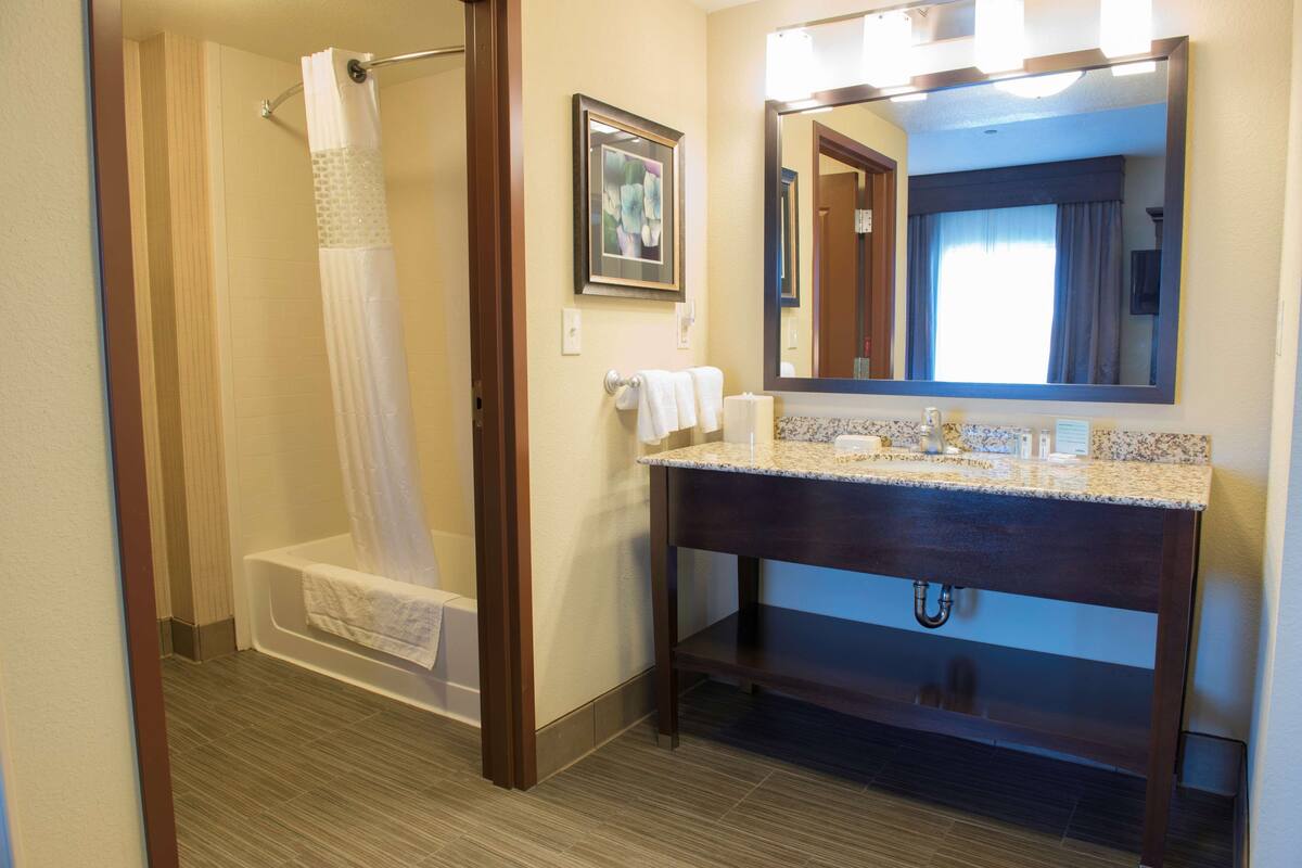 A bathroom with a shower, a sink with a mirror, and a towel rack.