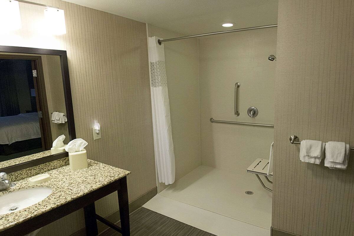 A hotel bathroom with a sink, mirror, shower, and towel rack.