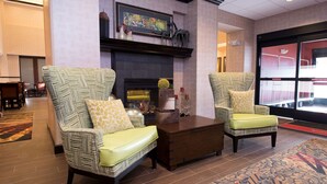 A lobby with two patterned armchairs, a wooden coffee table, a fireplace, and a large window. - Hampton Inn & Suites Bismarck Northwest (Bismarck)