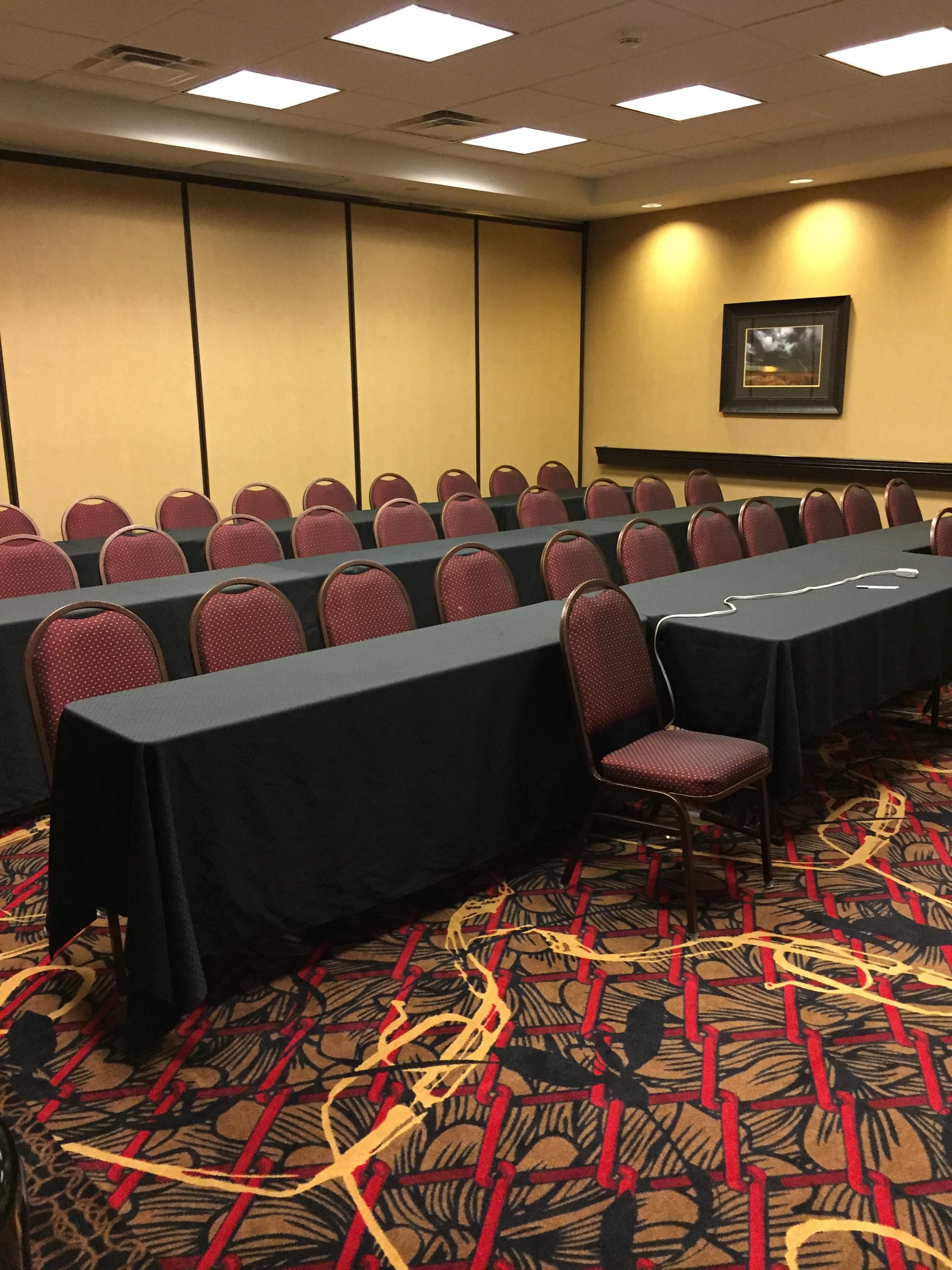 A conference room with rows of chairs and tables, carpeted floor, and ceiling lights.