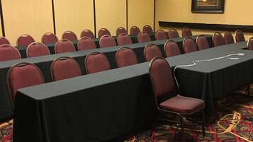 A conference room with rows of chairs and tables, carpeted floor, and ceiling lights.