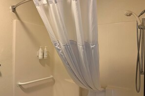 Un espace douche équipé d’un pommeau de douche mural blanc, d’un pommeau de douche à main et d’un rideau de douche.