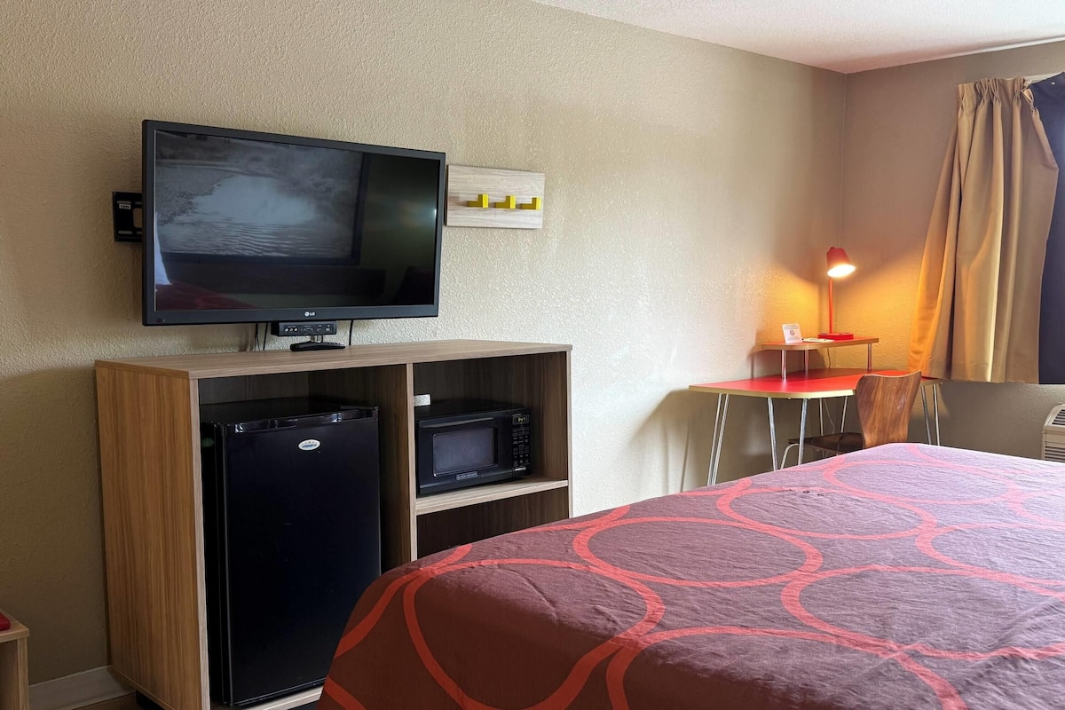 Une chambre d’hôtel équipée d’un lit, d’une télévision, d’un bureau avec une chaise, d’une lampe et d’un four à micro-ondes.