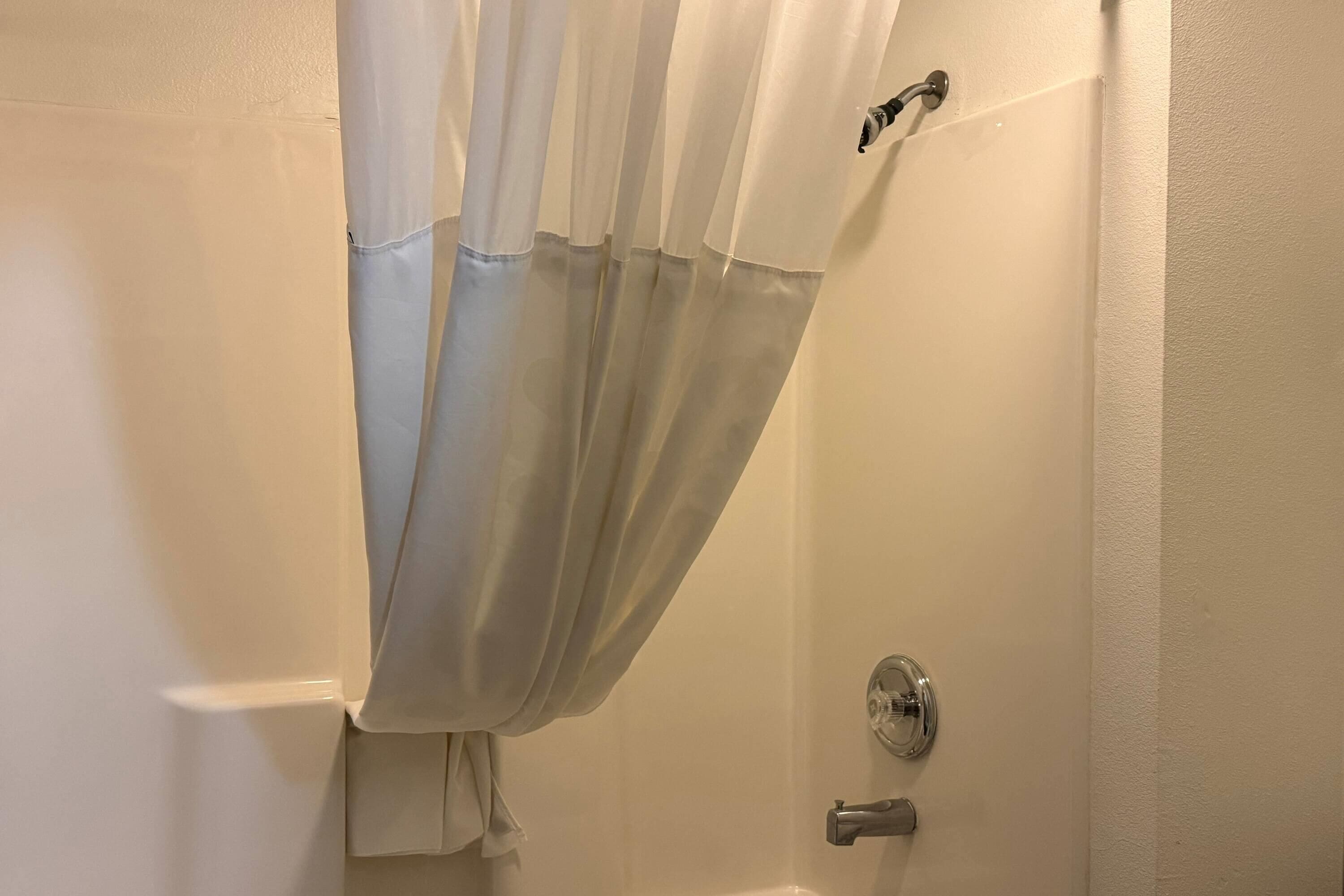 A bathroom with a white shower curtain, a showerhead, and a door handle.