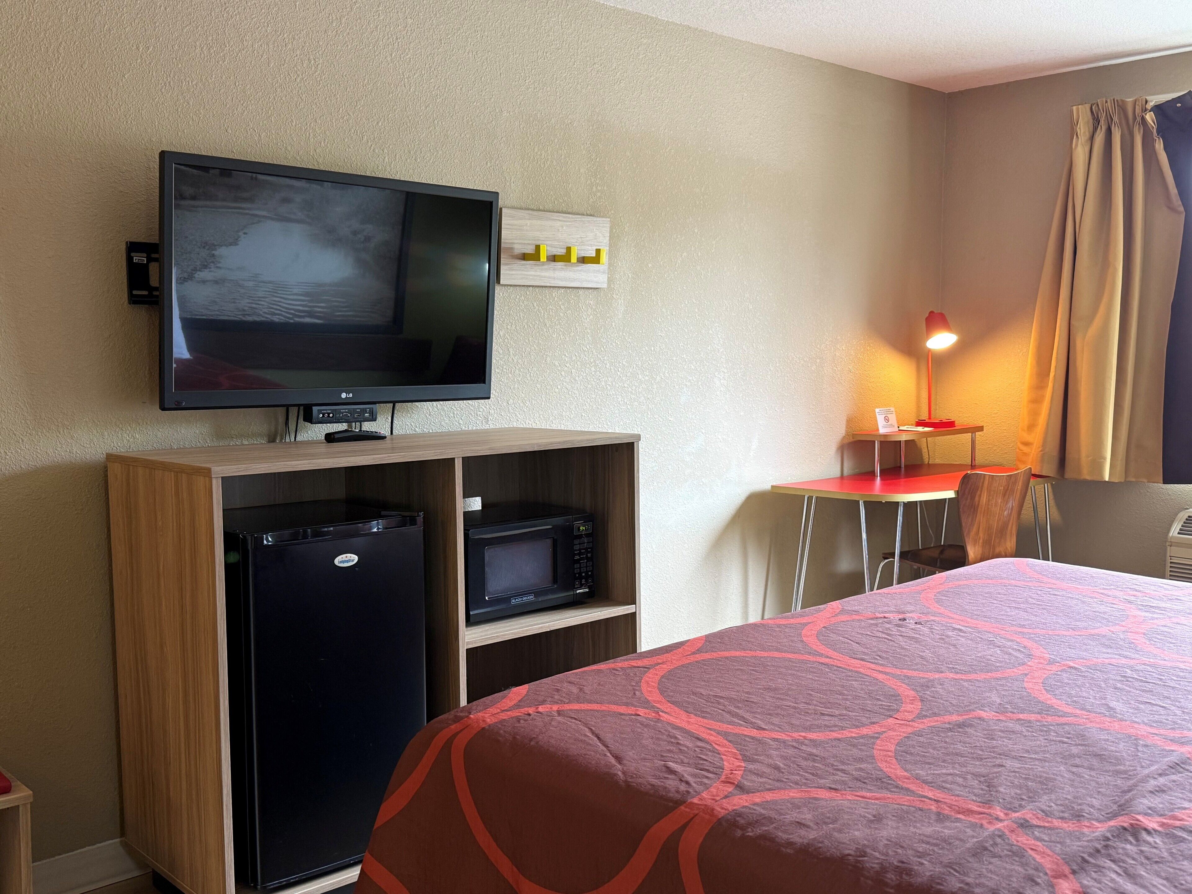 A hotel room with a bed, a desk, a chair, a television, a refrigerator, and a microwave.