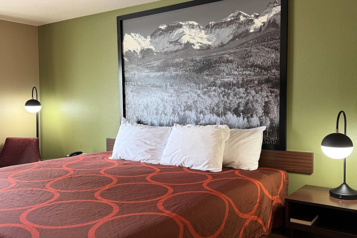 Une chambre d’hôtel avec un grand lit, deux lampes de chevet, un tableau représentant un paysage de montagne accroché au mur et un mur de couleur verte.