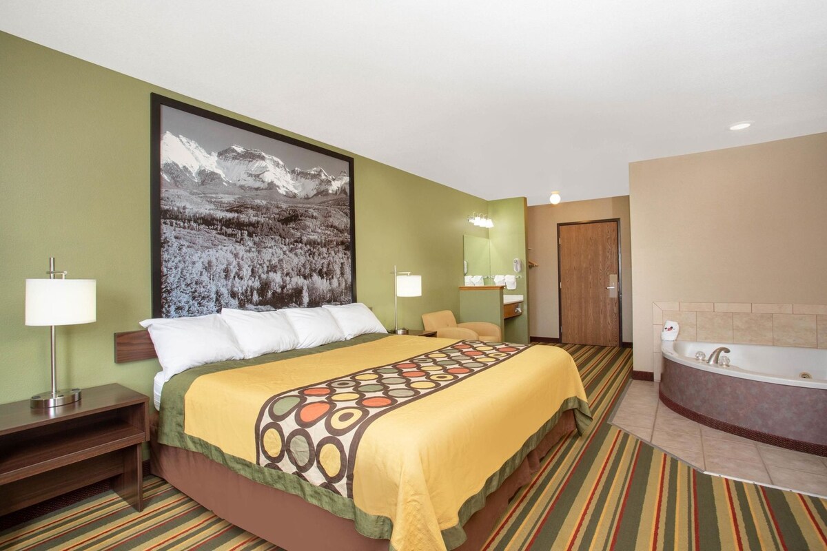 A hotel room with a large bed, a bathroom with a bathtub, a large window with a mountain view, and a green wall.