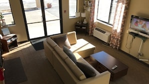 Una sala de estar con un sofá, una mesa de centro y un televisor. Hay una ventana con cortinas y una puerta que da al exterior.
