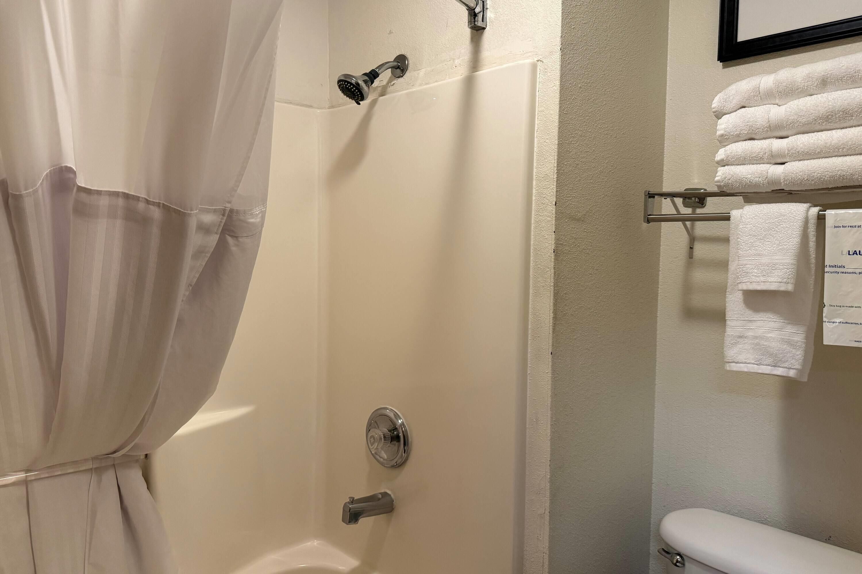 A shower with a curtain, a towel rack with folded towels, and a toilet.