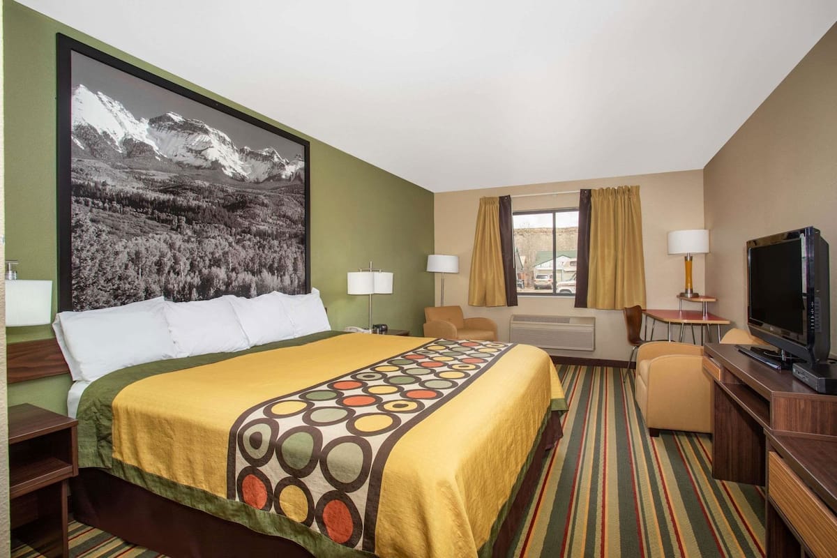 Une chambre d’hôtel avec un lit, une télévision, un bureau et une fenêtre avec des rideaux.