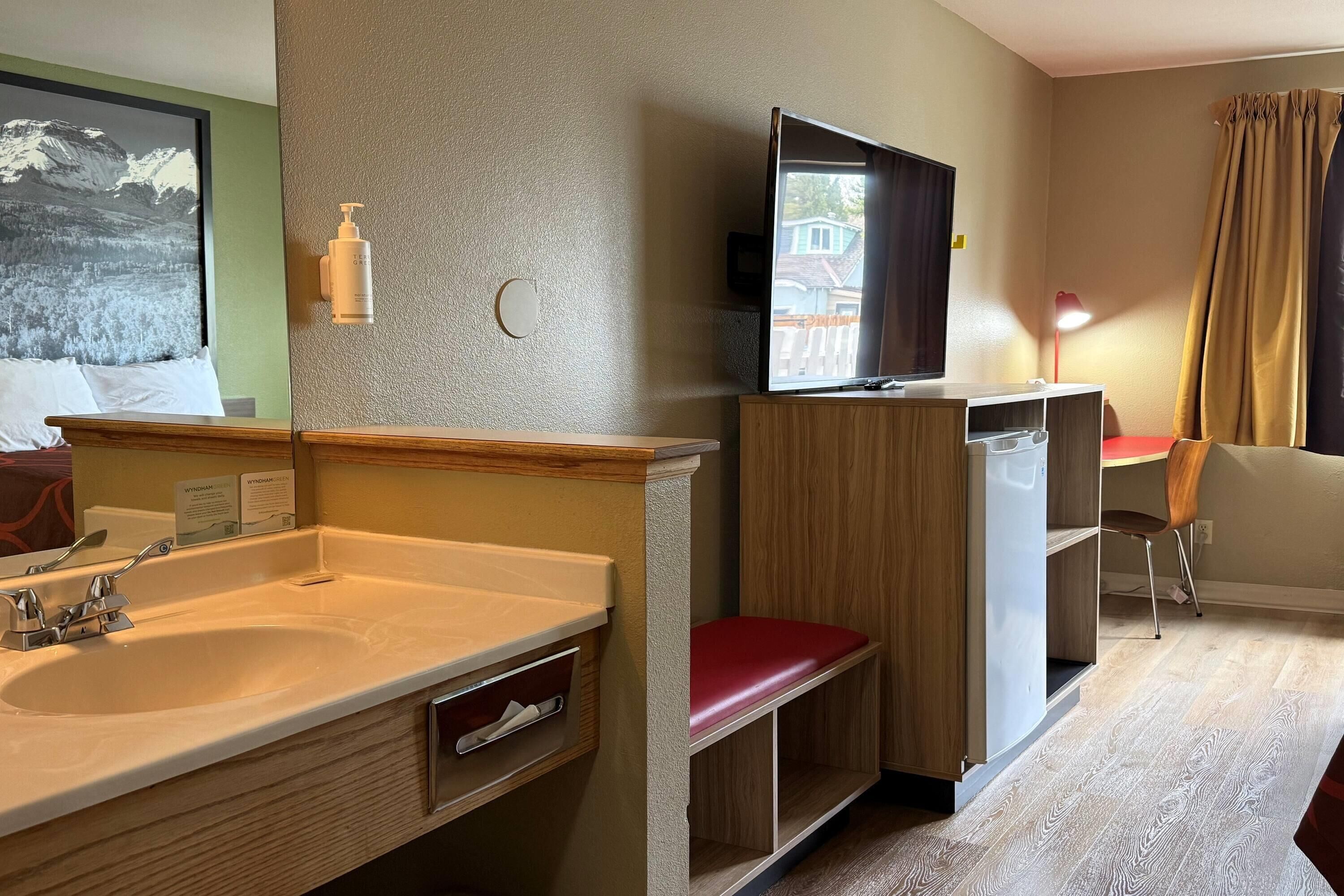 Habitación de hotel con lavabo, espejo, armario de madera, televisión y una silla.