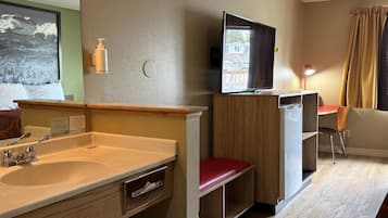 Habitación de hotel con lavabo, espejo, armario de madera, televisión y una silla.