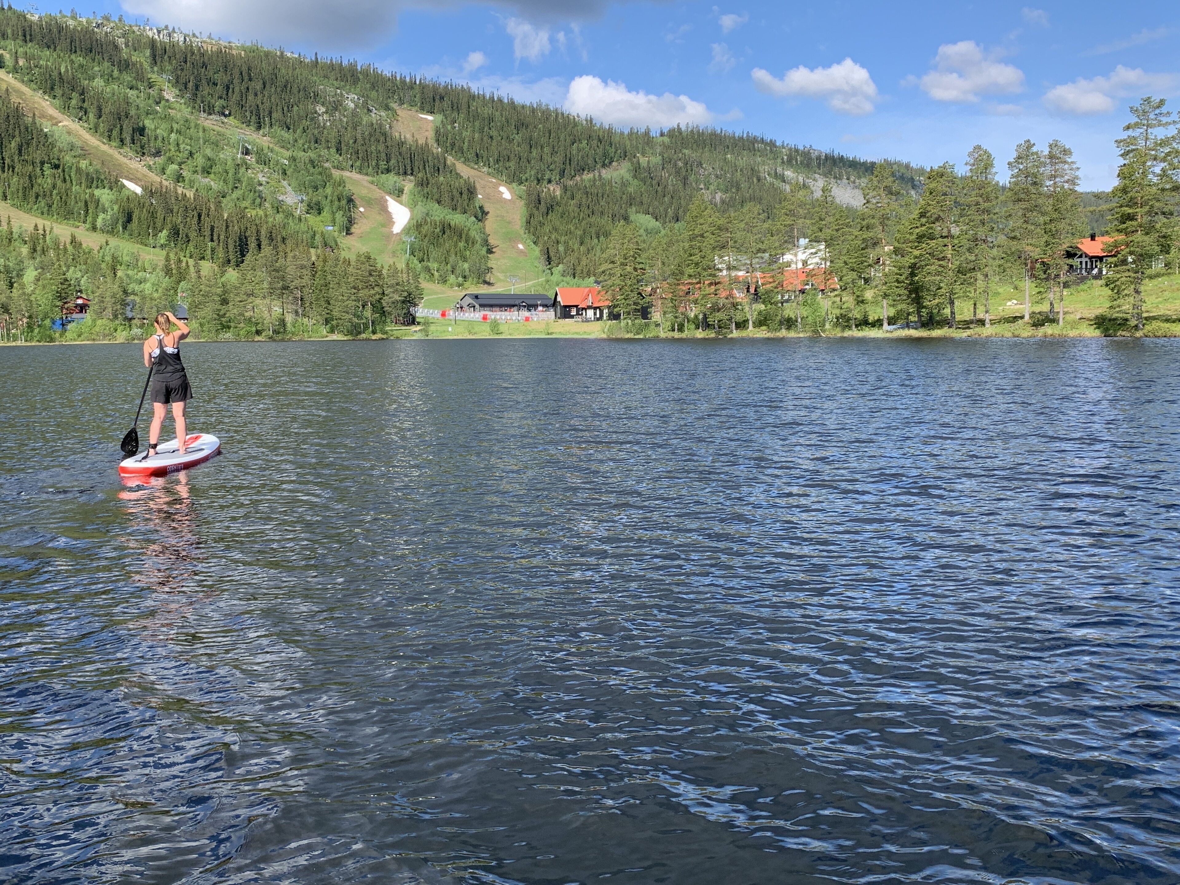 Una persona haciendo paddleboard en un lago tranquilo con montañas al fondo.