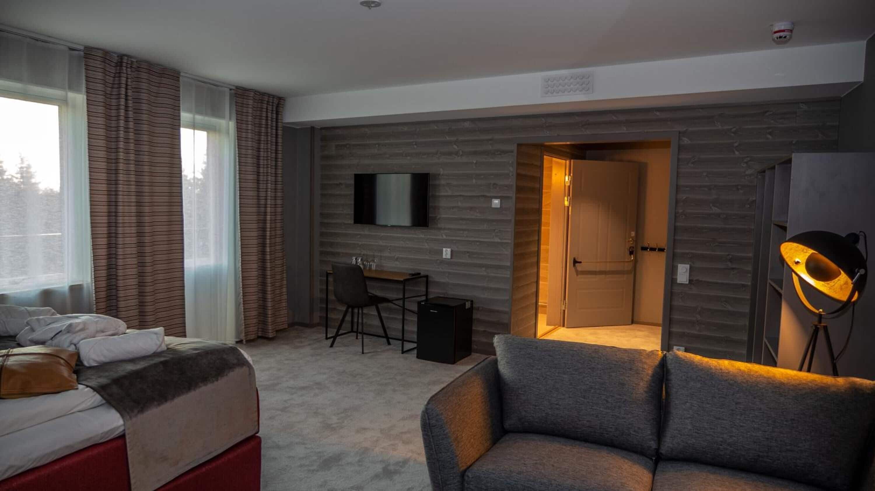 A hotel room with a bed, a desk, a chair, a TV, and a lamp.