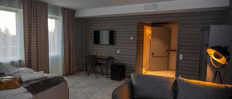 A hotel room with a bed, a desk, a chair, a TV, and a lamp.