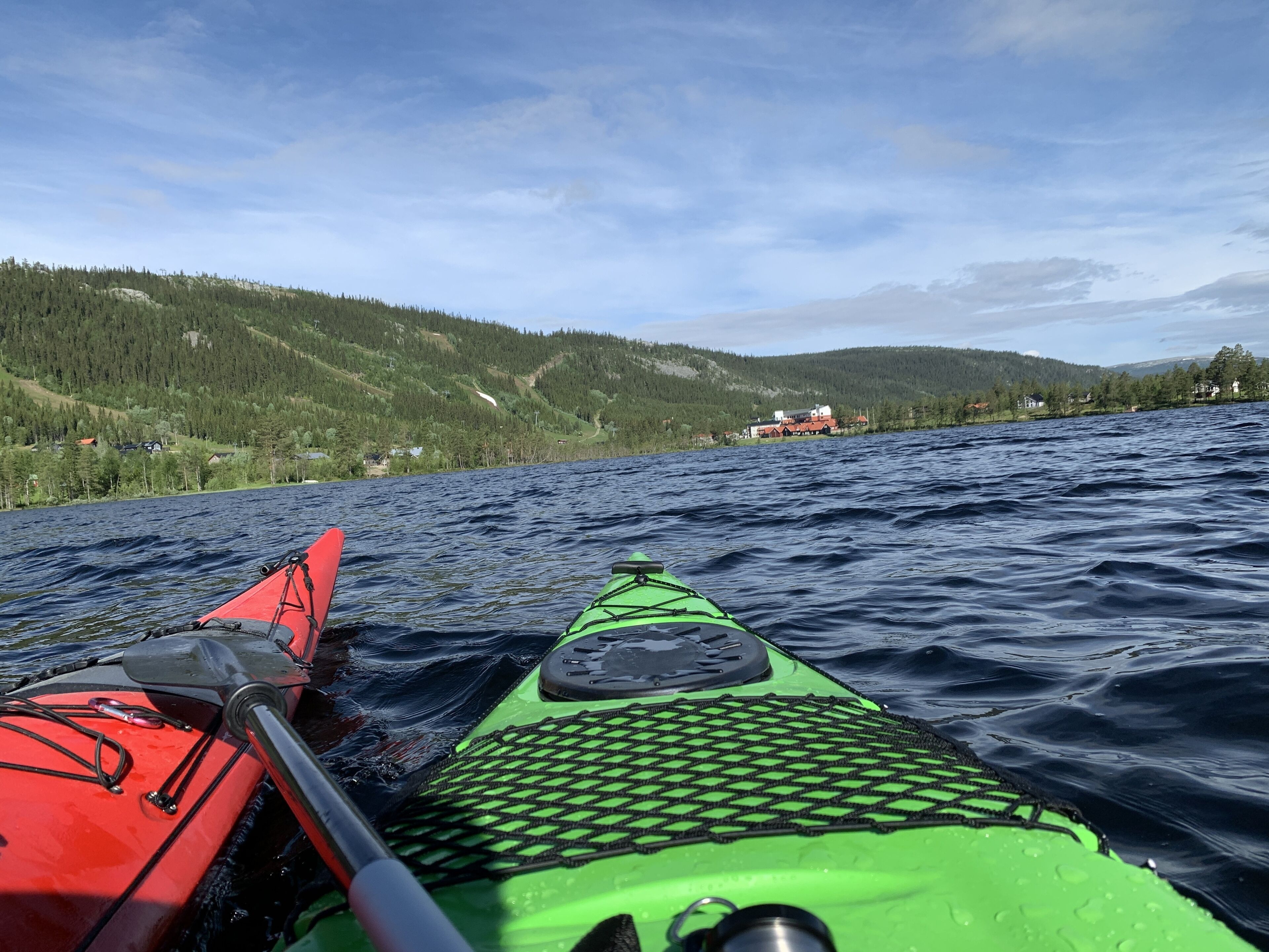 A kayak on a body of water with a forested shoreline and houses in the background.