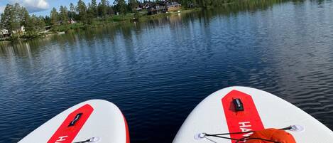Deux planches de paddle avec le mot « HAYES » écrit dessus, un lac paisible et une rive boisée avec des maisons en arrière-plan.
