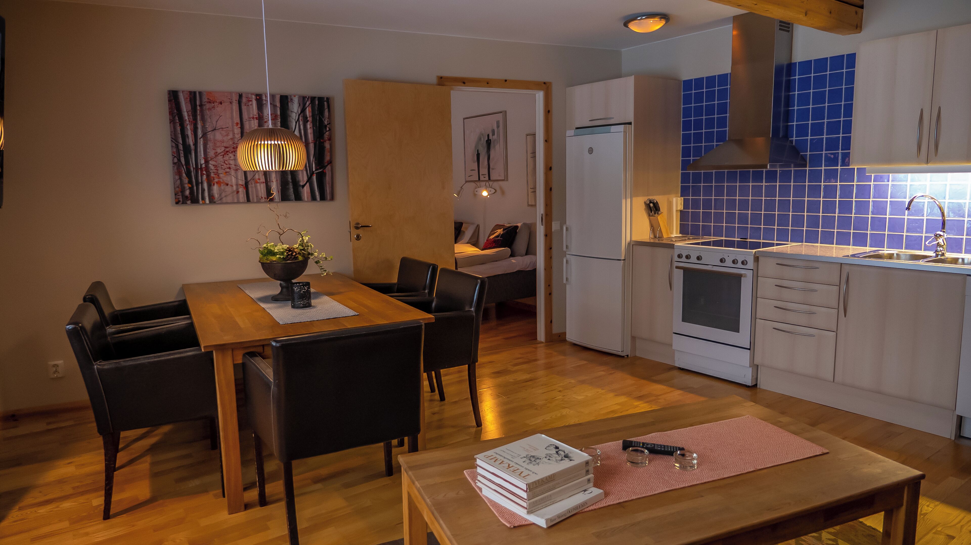 Una cocina compacta con estufa, horno y pileta. Hay un comedor con mesa y sillas, y una pequeña sala de estar con sofá.