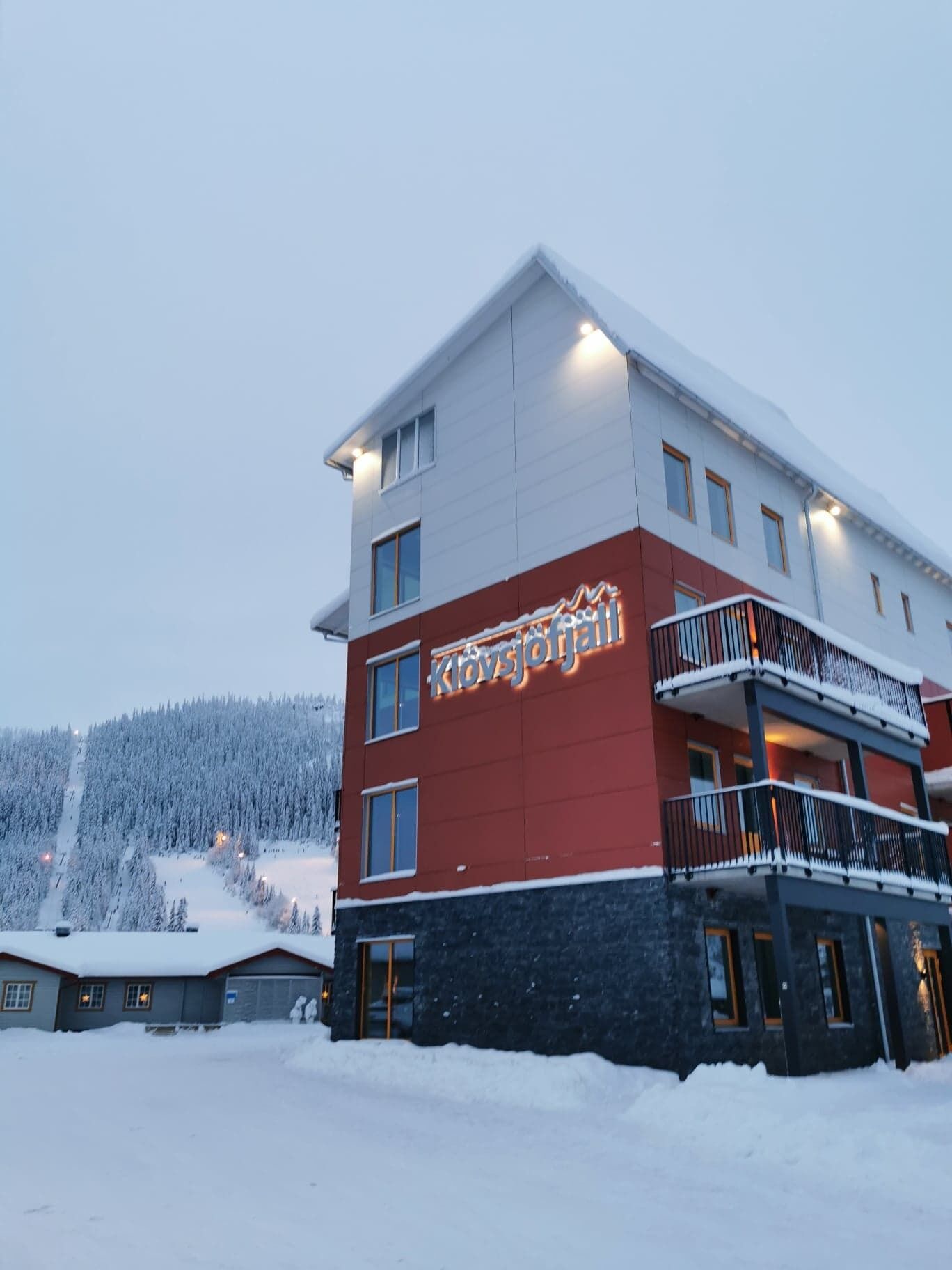 A multi-story hotel with a red and white facade, balconies, and a sign reading "Klövsjöbad."