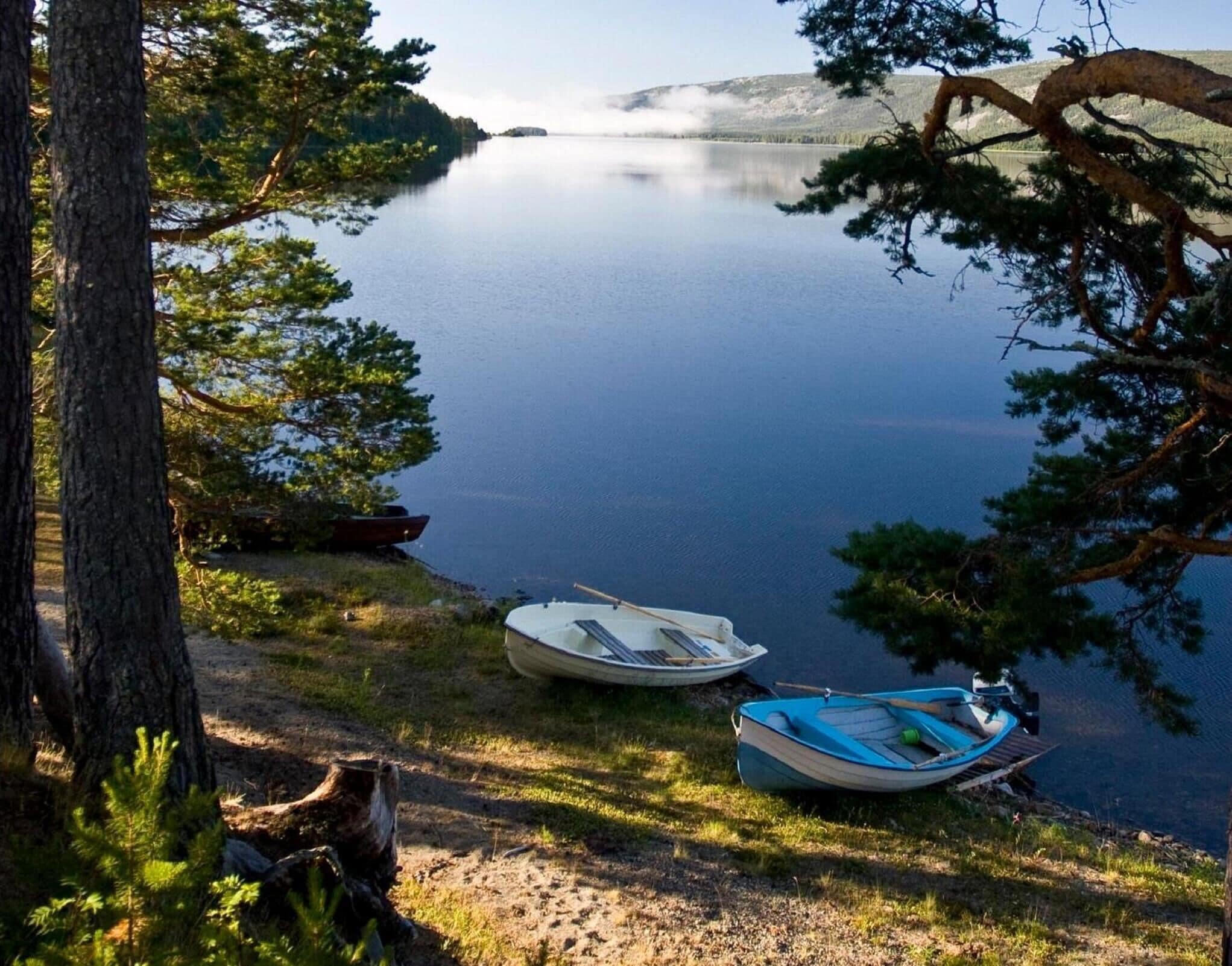 A serene lakeside scene with two boats docked near the shore, surrounded by trees and a clear view of the lake.