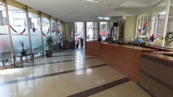 A hotel lobby with a reception desk, a potted plant, and a tiled floor.