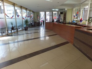 A hotel lobby with a reception desk, a potted plant, and a tiled floor. - Andino Departamentos (Santiago)