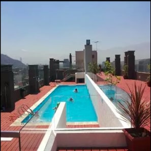A rooftop pool with clear blue water, surrounded by red-tiled flooring and potted plants. - Andino Departamentos (Santiago)