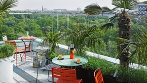 En tagterrasse med et bord og stole, omgivet af vegetation og udsigt over bybilledet.
