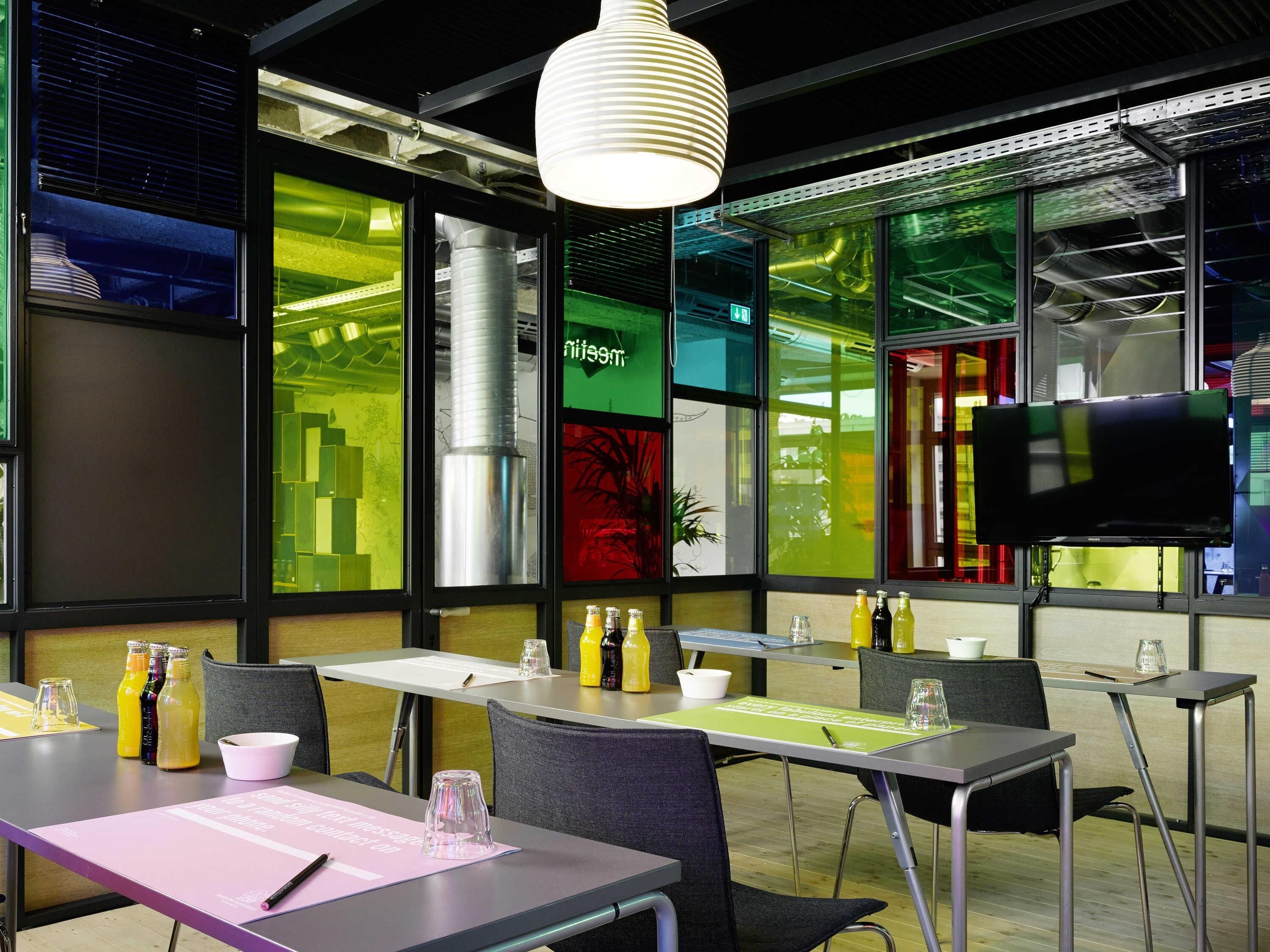 Una sala conferenze moderna con tavoli, sedie, un grande schermo e un originale design della finestra con verde e giallo.