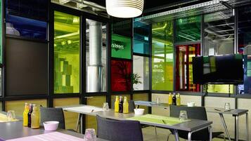 Una sala conferenze moderna con tavoli, sedie, un grande schermo e un originale design della finestra con verde e giallo.