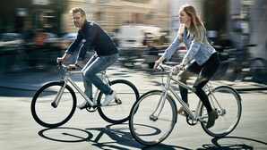To personer cykler på en gade i byen.