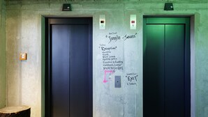 To elevatorporte med graffiti og håndskrevne noter, der angiver vejvisning til forskellige steder i bygningen.